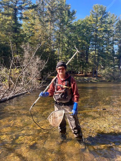 Graduate student Michael Trapp poses in a stream with a net and backpack electrofishing gear.